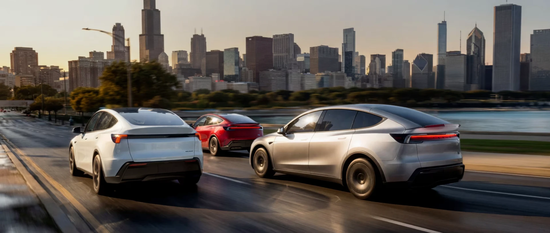 Three Tesla Model Y vehicles driving along a city waterfront at sunset